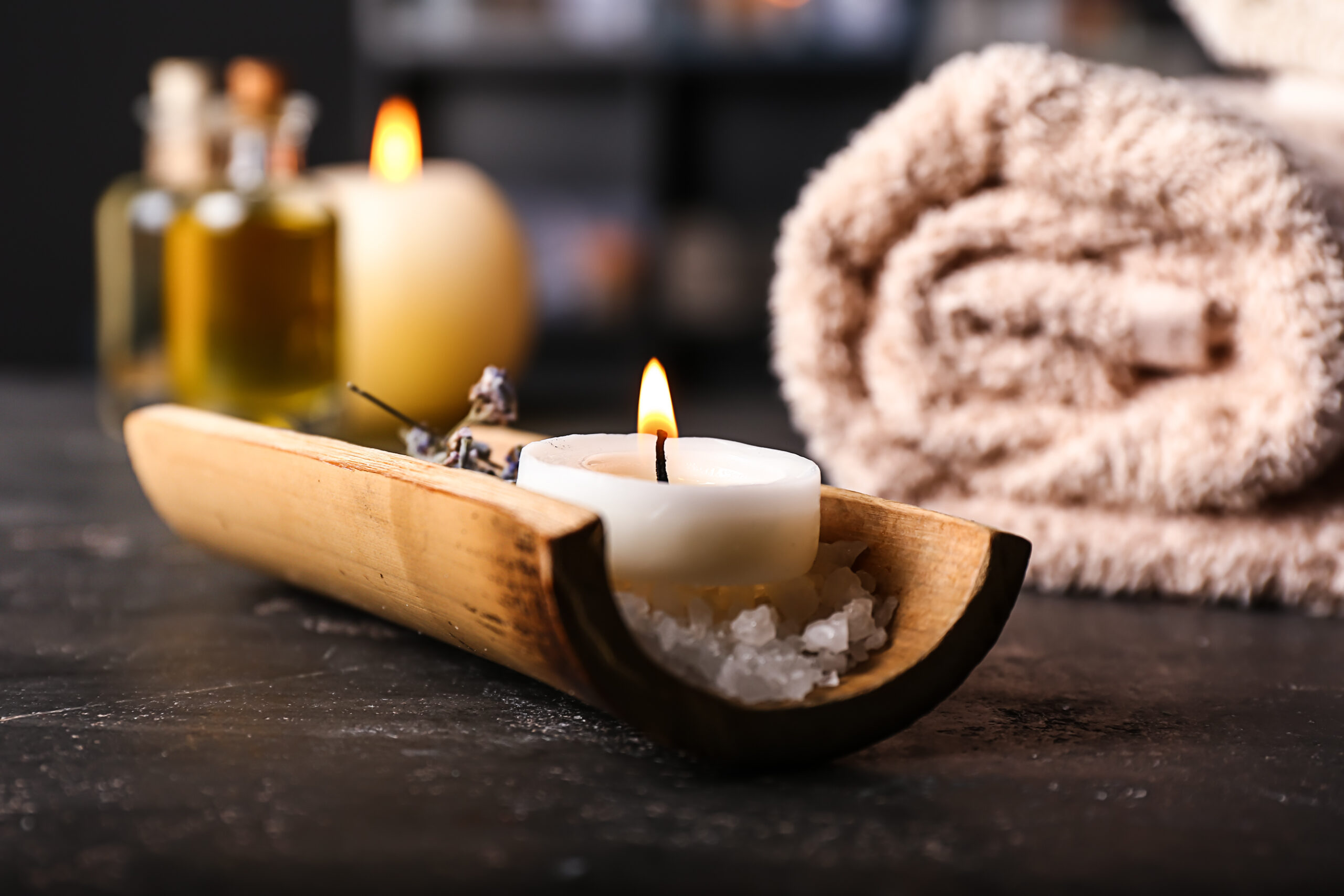A photo of items you would find at a spa, included soaps, rock salt, bath oils, towels and a burning candle.