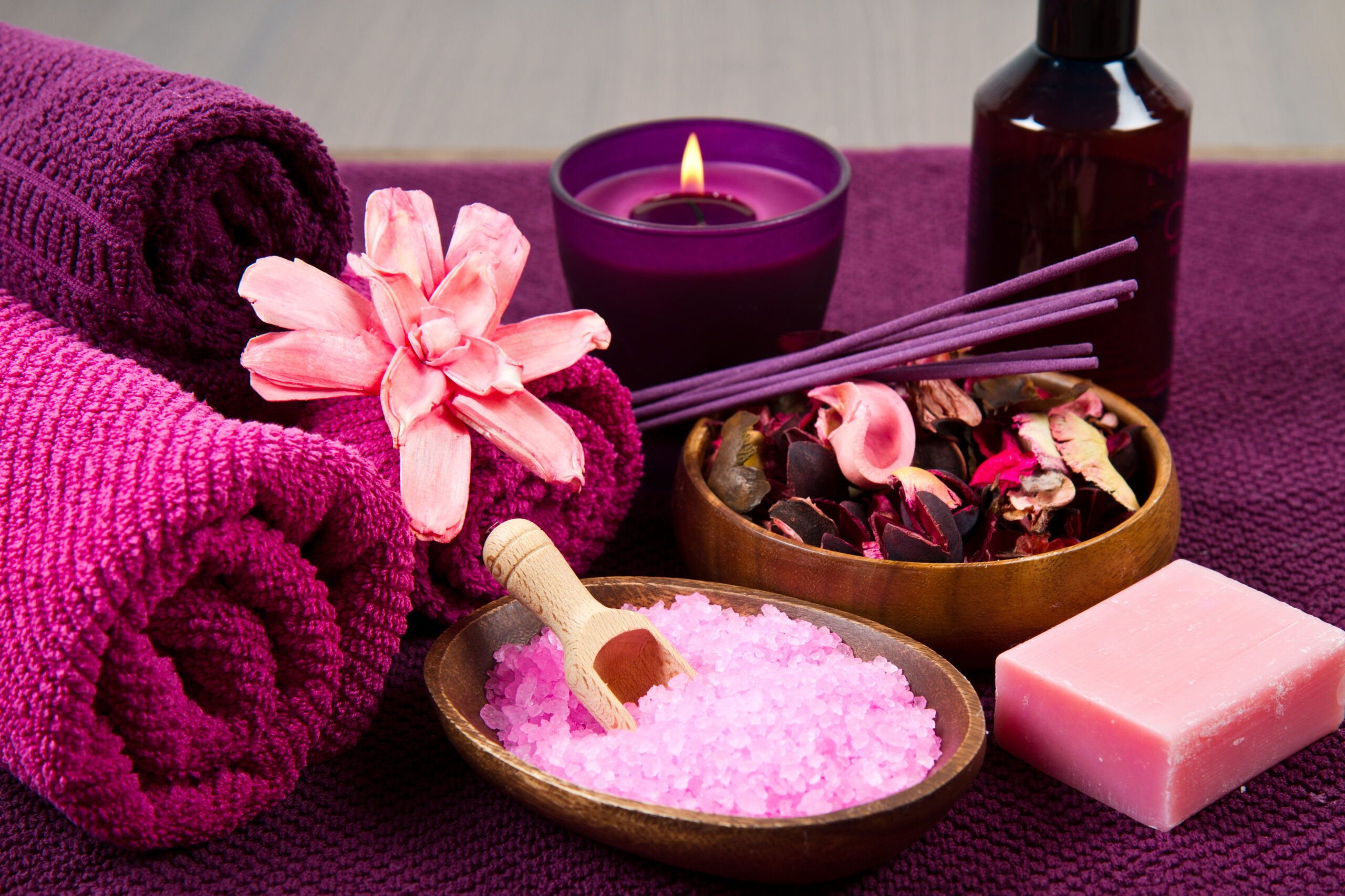 A photo of items you would find at a spa, included soaps, rock salt, bath oils, towels and a burning candle.
