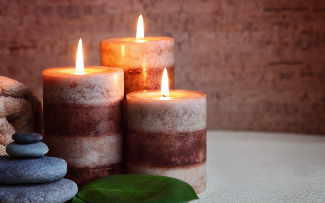 lit candles with smooth hot stones on a massage table with a folded towel